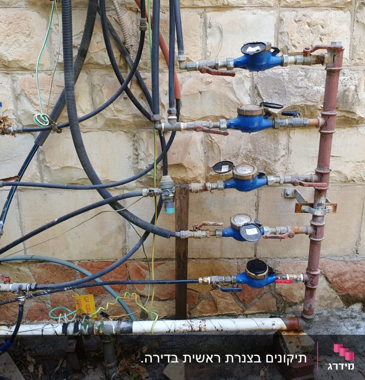 מד מים כחולים וצינורות מחוברים לקיר אבן